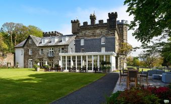 a large , stone castle - like building with a stone foundation and multiple windows , surrounded by green grass and trees at Portmeirion Village & Castell Deudraeth