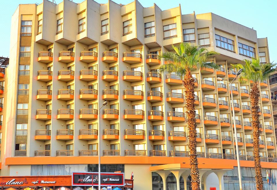 a large building with many balconies and palm trees in front of a store with colorful signs at Aracan Pyramids Hotel