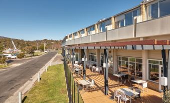 a modern building with large windows and wooden floors , surrounded by trees and benches on a sunny day at Bayside Hotel