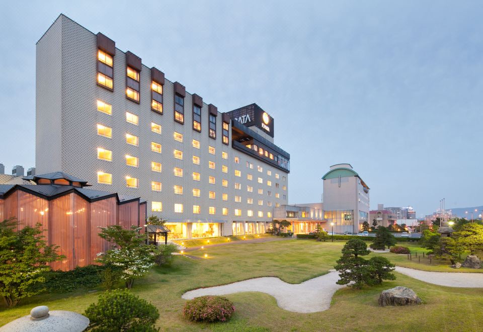 a large hotel with a gray exterior and large windows is surrounded by a well - maintained lawn at Hotel Ichibata