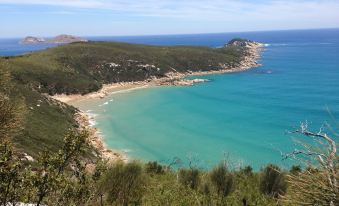 a picturesque view of a turquoise sea with a sandy beach , surrounded by lush green hills at Prom Coast Holiday Lodge