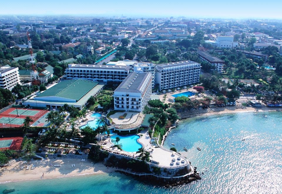 a large hotel surrounded by palm trees and a body of water , possibly an ocean or a lake at Dusit Thani Pattaya