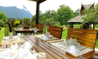 an outdoor dining area with wooden tables and chairs set up for a meal , surrounded by trees and mountains at Aurora Resort Chiangdao
