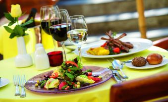 a table is set with plates of food , wine glasses filled with wine , and a yellow tablecloth at Dalyan Live Spa Hotel