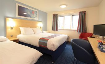 a hotel room with two beds , a window , and a chair , all decorated in white and blue colors at Travelodge Stonehouse