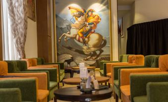 a large painting of a man riding a horse is displayed in an empty room with green chairs and tables at Z Hotel