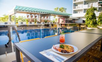 a poolside dining area with a table full of food , including a plate of breakfast items , and a view of the pool at Rydges Palmerston - Darwin, an EVT hotel