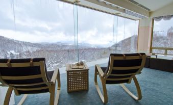 two wooden rocking chairs placed in front of a large window , overlooking a snowy mountain landscape at Arcadia