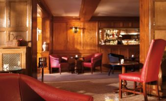 a cozy bar with red leather chairs , wooden walls , and a piano , creating a warm and inviting atmosphere at Macdonald Compleat Angler