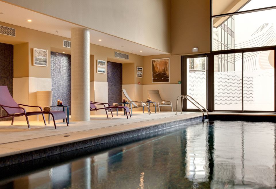 an indoor swimming pool with a large window , surrounded by lounge chairs and tables , creating a relaxing atmosphere at Renaissance Aix-en-Provence Hotel