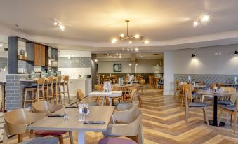 a modern , well - lit restaurant with wooden floors and large windows , featuring multiple dining tables and chairs arranged in a spacious room at Holiday Inn Ipswich