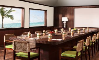 a large dining table set with plates , cups , and utensils in a room with wooden walls and windows at Taj Exotica Resort & Spa