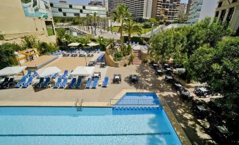 a large outdoor pool surrounded by lounge chairs and umbrellas , with a city skyline in the background at Hotel Bristol 4 Sup