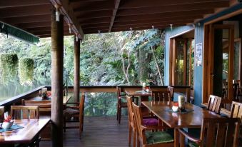 a wooden dining area with tables and chairs , surrounded by a lush green forest backdrop at Rainforest Eco Lodge