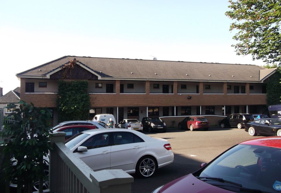 a long building with a sloping roof , surrounded by cars parked in front of it at Richmond Park Hotel