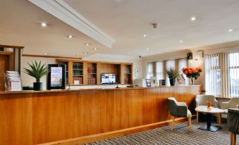 a hotel lobby with a wooden reception desk and chairs , as well as various plants and flowers at Best Western Bradford Guide Post Hotel