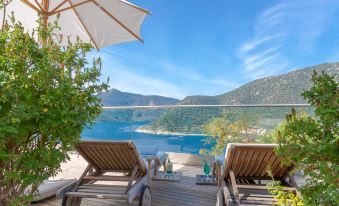 a wooden deck overlooking a beautiful lake , with two lounge chairs and an umbrella providing shade at Happy Hotel Kalkan