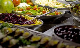 a variety of dishes , including salads and fries , are displayed on a buffet table with forks nearby at Maun Lodge