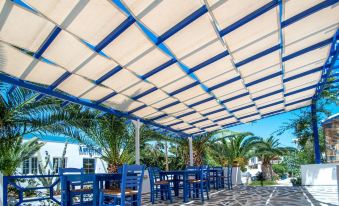 a blue and white striped awning over a patio area with tables and chairs under it at Syros Atlantis