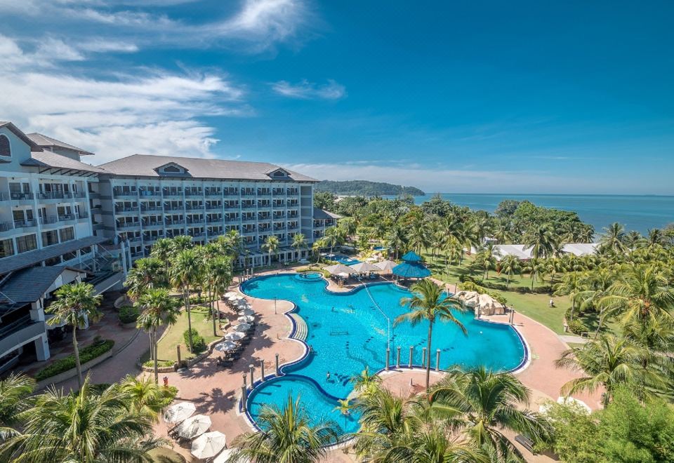 a large hotel with a swimming pool surrounded by palm trees , providing a picturesque view of the ocean at Thistle Port Dickson Resort