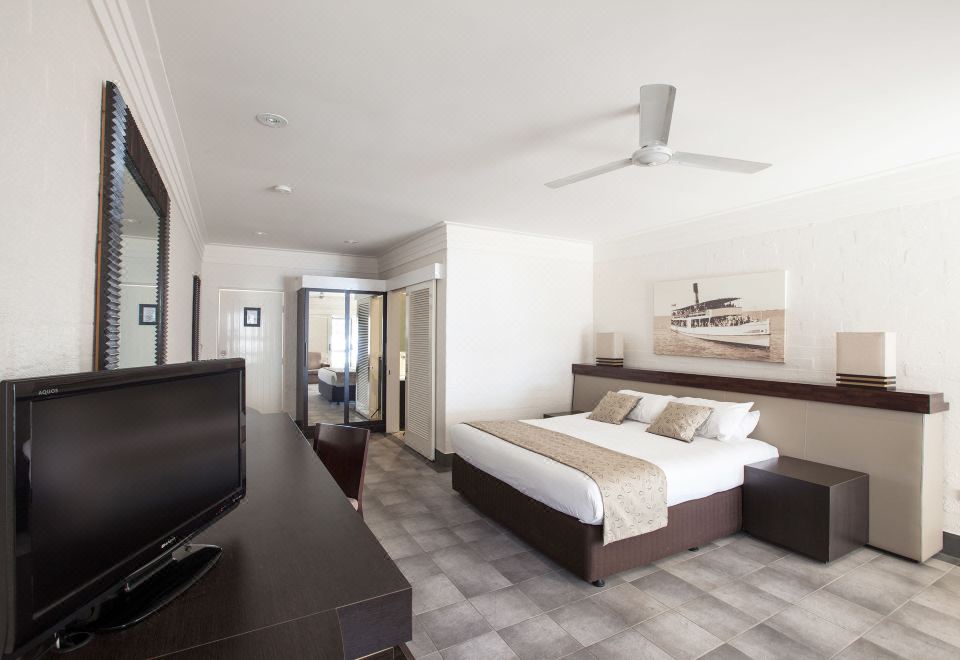 a spacious bedroom with a king - sized bed , a flat - screen tv mounted on the wall , and a dresser nearby at Karma Rottnest