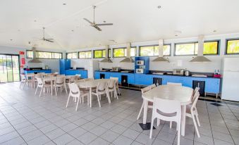 a large , open kitchen with blue cabinets and white chairs , along with a dining area at Discovery Parks - Ballina