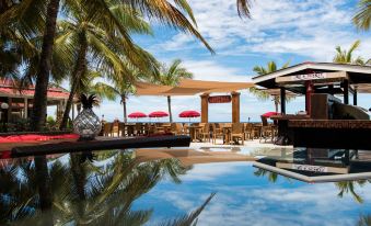 a tropical resort with a pool surrounded by palm trees , umbrellas , and a dining area at Bohio Dive Resort
