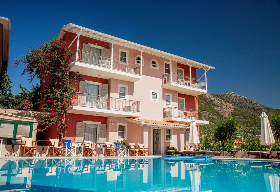 a large pink house with a swimming pool in front of it , surrounded by grass and trees at G George