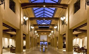 a large , well - lit hallway with high ceilings and a checkered floor , leading to an entrance at Kempinski Hotel Ishtar Dead Sea