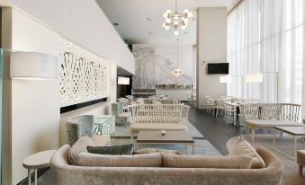 a modern , well - lit living room with white walls and furniture , including a couch , chairs , and dining table at NH Parma