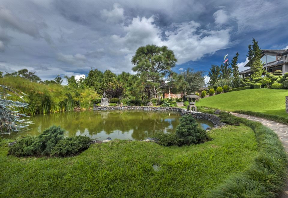 a serene pond surrounded by lush green grass and trees , with a gazebo in the background at Koanze Luxury Hotel & Spa