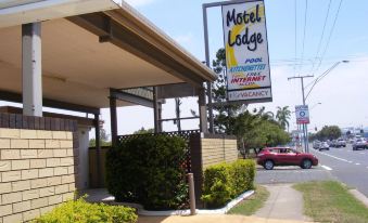 a motel sign is hanging from the side of a building , with a car parked in front of it at Motel Lodge