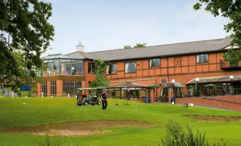 a golf course with a building in the background , surrounded by trees and grass , under a clear blue sky at Macdonald Hill Valley Hotel Golf & Spa