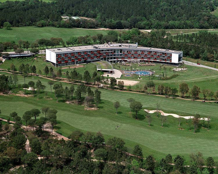 an aerial view of a golf course with a large building in the background , surrounded by trees at Camiral Golf & Wellness - Leading Hotel of the World