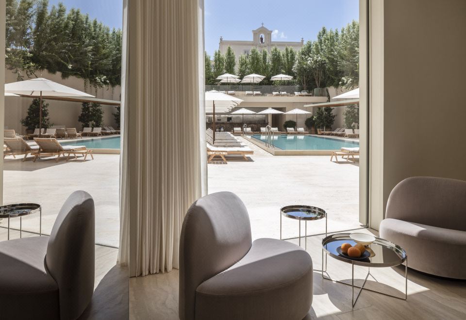 a luxurious hotel room with a large window overlooking a swimming pool , sun loungers , and umbrellas at The Jaffa, a Luxury Collection Hotel, Tel Aviv
