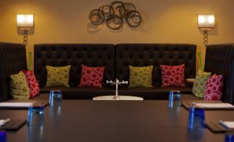 a long black couch with multiple colorful pillows is facing a long table with blue glassware at Washington Dulles Airport Marriott