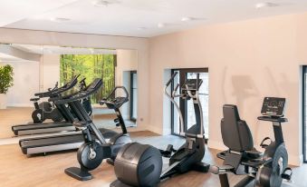 a gym room with various exercise equipment , including a treadmill , an elliptical machine , and a stationary bike at NH Leipzig Zentrum