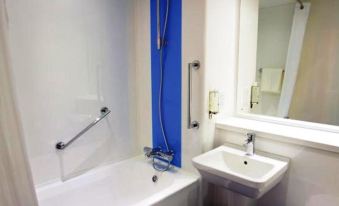 a small bathroom with a bathtub , toilet , sink , and mirror , as well as blue curtains on the window at Travelodge Southport