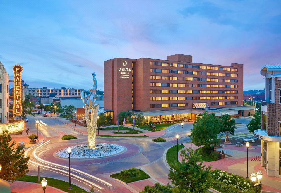 a large hotel with a fountain in front of it , surrounded by trees and buildings at Delta Hotels Muskegon Convention Center