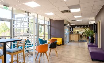 a modern office space with colorful chairs and tables , large windows , and a reception area at Comfort Hotel Aeroport Lyon St Exupery