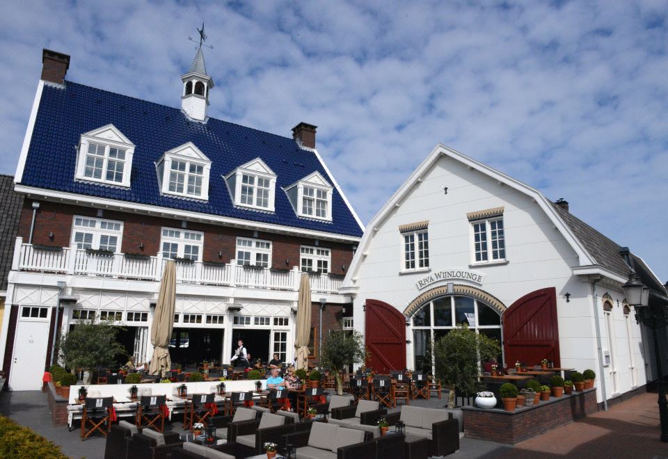 a large white building with a blue roof and red doors is surrounded by other buildings at Fletcher Hotel - Restaurant Nautisch Kwartier