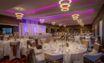 a well - decorated banquet hall with multiple tables set for a formal event , including white tablecloths and gold chairs at Clayton Hotel Chiswick
