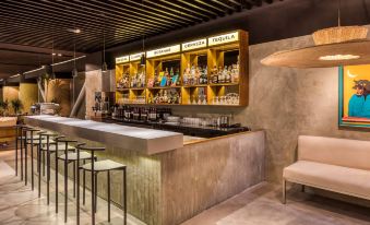 a modern bar with a wooden counter , multiple stools , and shelves filled with various bottles at Le Meridien Mexico City
