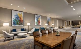 a large , modern hotel lobby with a wooden table and chairs , comfortable seating , and colorful paintings on the walls at Fairmont Dallas