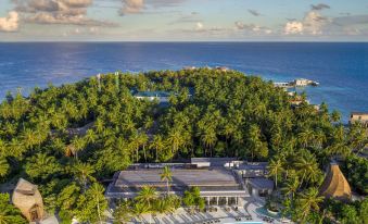 an aerial view of a resort with a pool surrounded by palm trees and lush greenery , with the ocean in the background at The St. Regis Maldives Vommuli Resort
