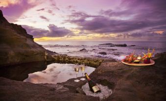 a romantic scene with a bottle of wine and two glasses placed on rocks near the ocean at Cap Maison Resort & Spa