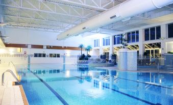 an indoor swimming pool surrounded by a building , with several people enjoying their time in the pool at Village Hotel Cardiff