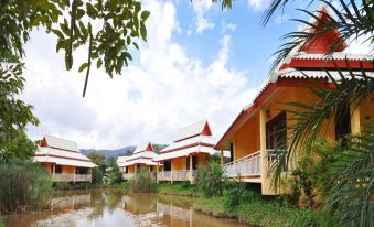 a row of small wooden houses with a red roof are situated next to a body of water at Poonyamantra Resort