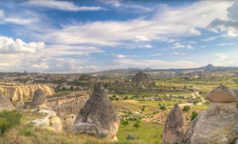 a panoramic view of a mountainous landscape with various rock formations and grassy plains under a blue sky dotted with clouds at Azure Cave Suites - Cappadocia