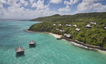 aerial view of a tropical island with multiple thatched - roof cabins situated on the shore of the ocean at Mandarin Oriental, Canouan